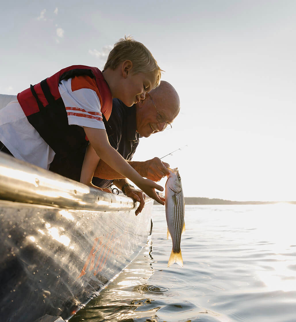 A bald man and his grandson lean over the side of their boat to examine a fish they've caught.