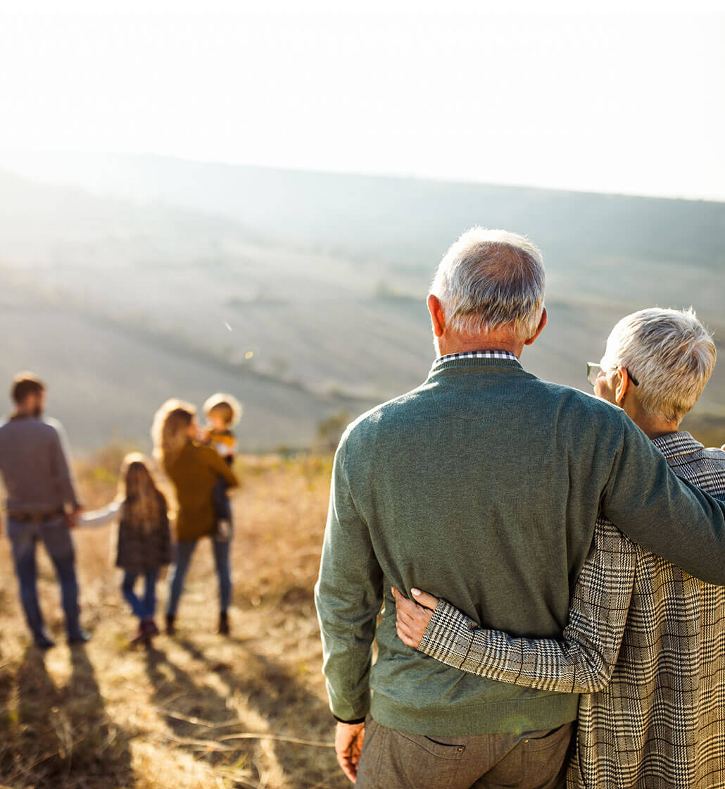 A couple and their grand children are facing away from the camera. They are jumping in the air and holding hands.